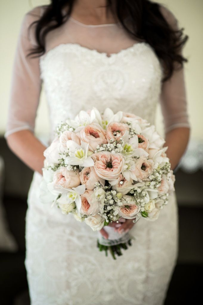 La sposa, con indosso un abito da sposa di pizzo, tiene in mano un bouquet rosa pallido e bianco.