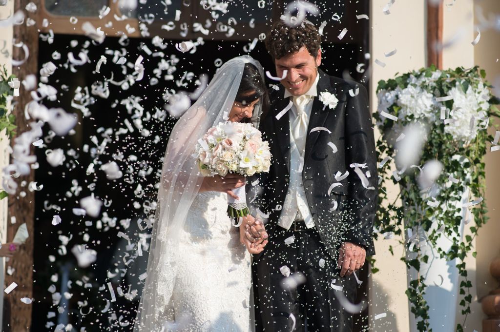 Gli sposi tra una pioggia di coriandoli, la sposa tiene in mano il bouquet e lo sposo sorride in abito elegante.