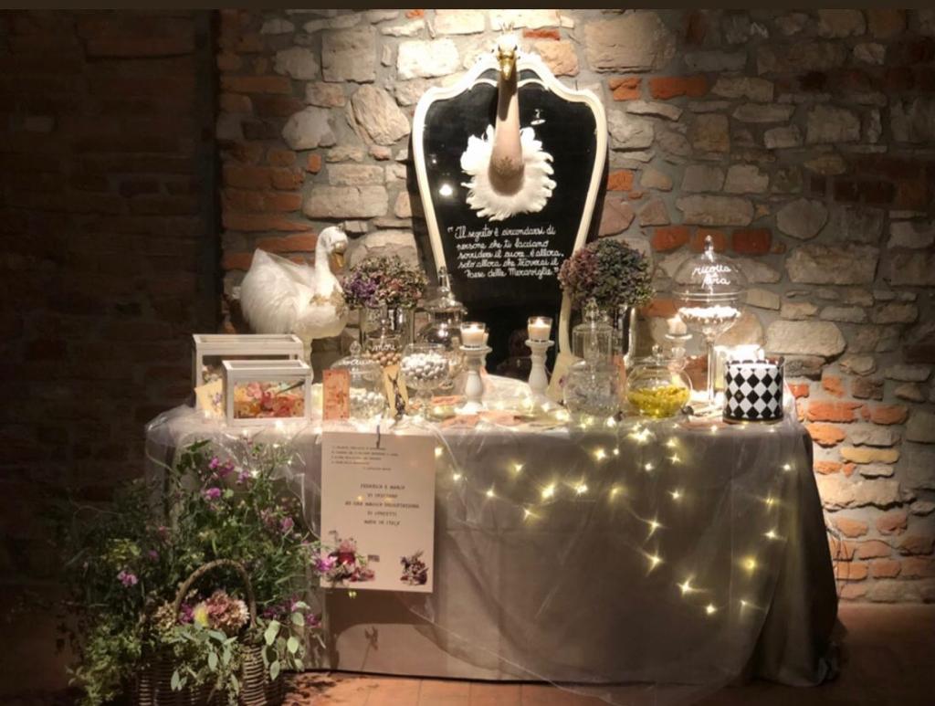 Altare commemorativo con candele, fiori e lucine, addossato a un muro di mattoni.