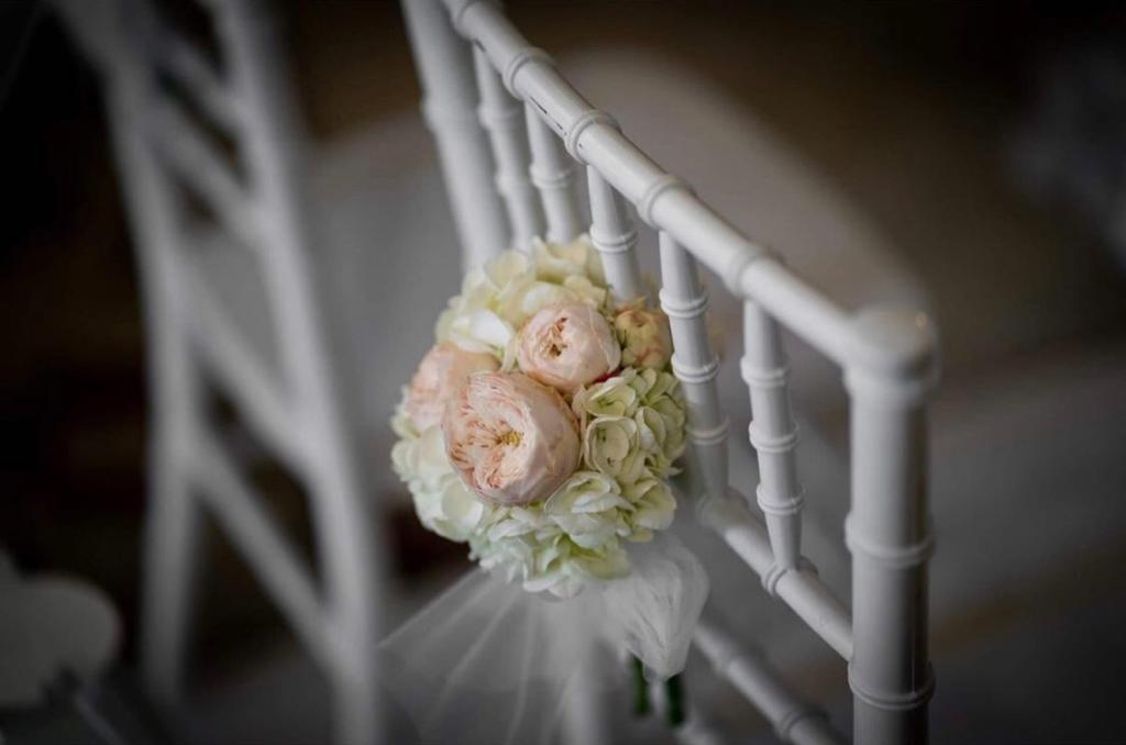 Bouquet da sposa dai colori pastello appeso a una sedia bianca, sfocato.
