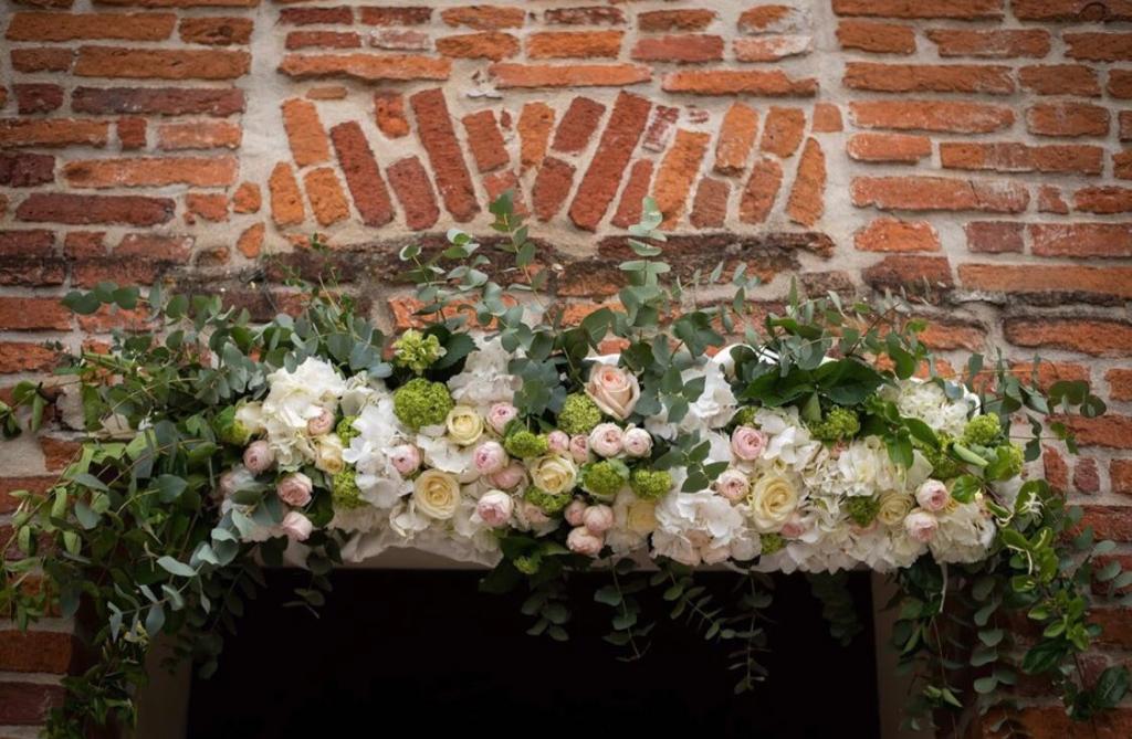 Ghirlanda floreale di fiori bianchi, rosa e verdi drappeggiata sul caminetto in mattoni.