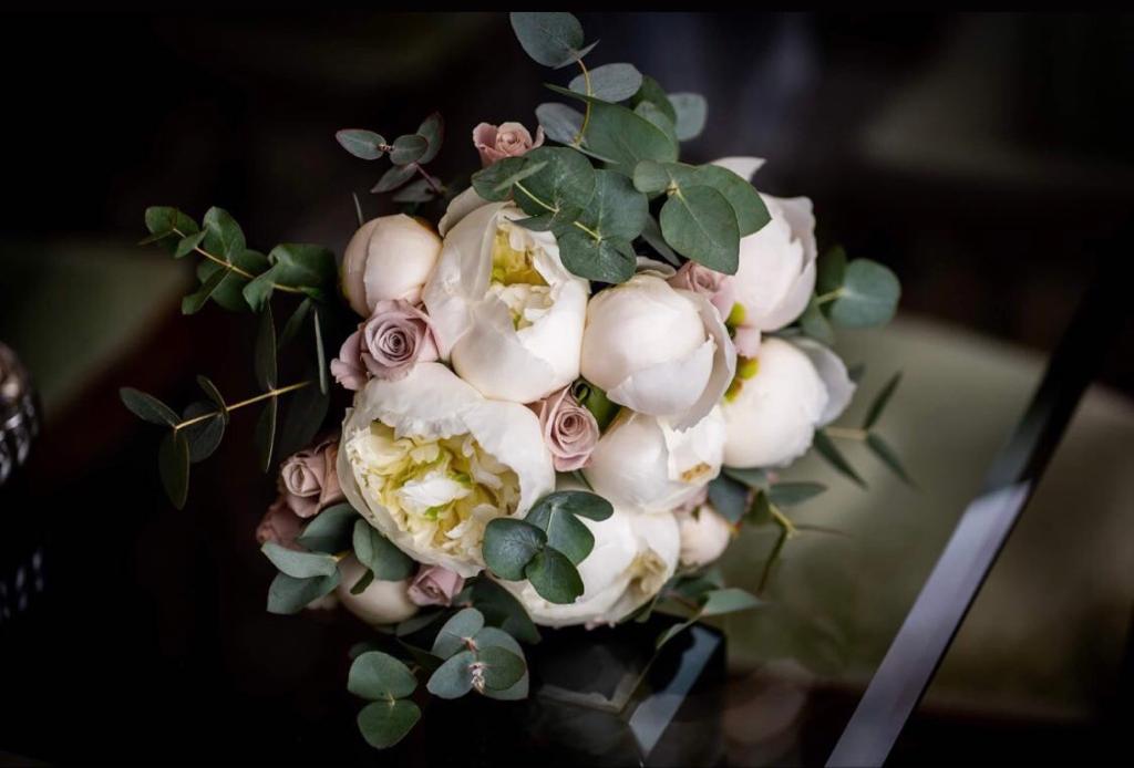 Bouquet floreale bianco e rosa con eucalipto verde su una superficie scura riflettente