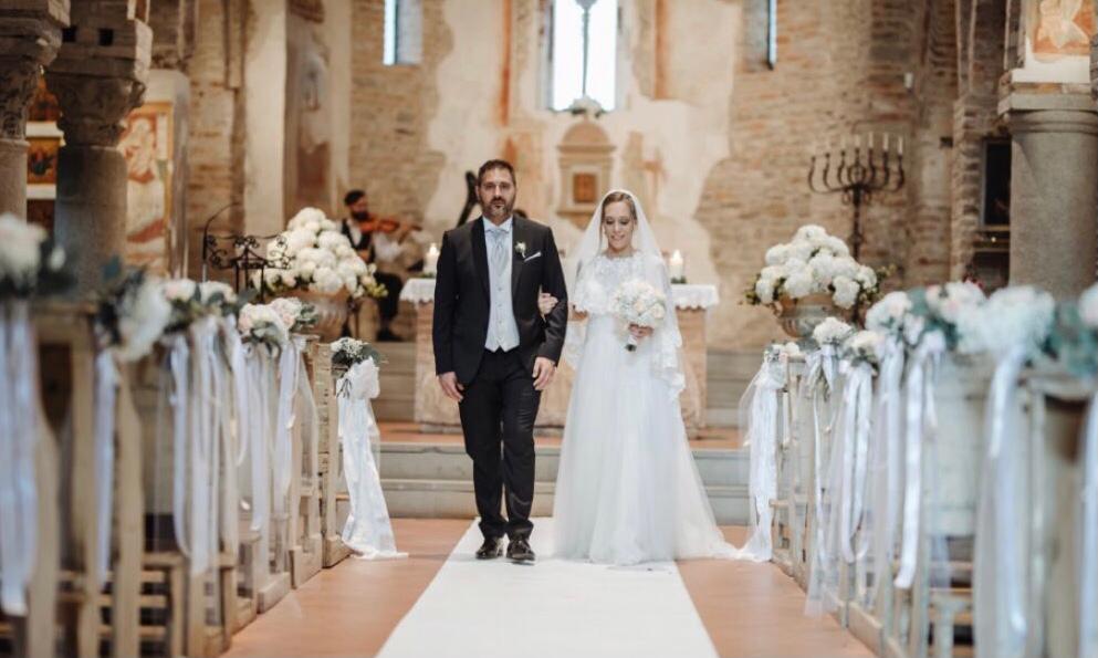 Gli sposi percorrono una navata fiancheggiata da fiori durante una luminosa cerimonia nuziale in chiesa.