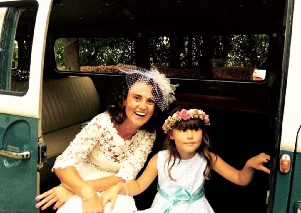 Una donna e una ragazzina in abiti femminili siedono in macchina, sorridono e indossano corone di fiori.