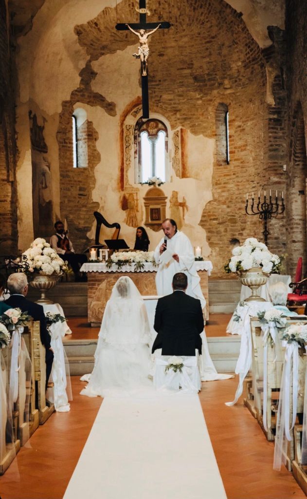 Cerimonia nuziale in chiesa, con gli sposi all'altare tra fiori bianchi e banchi