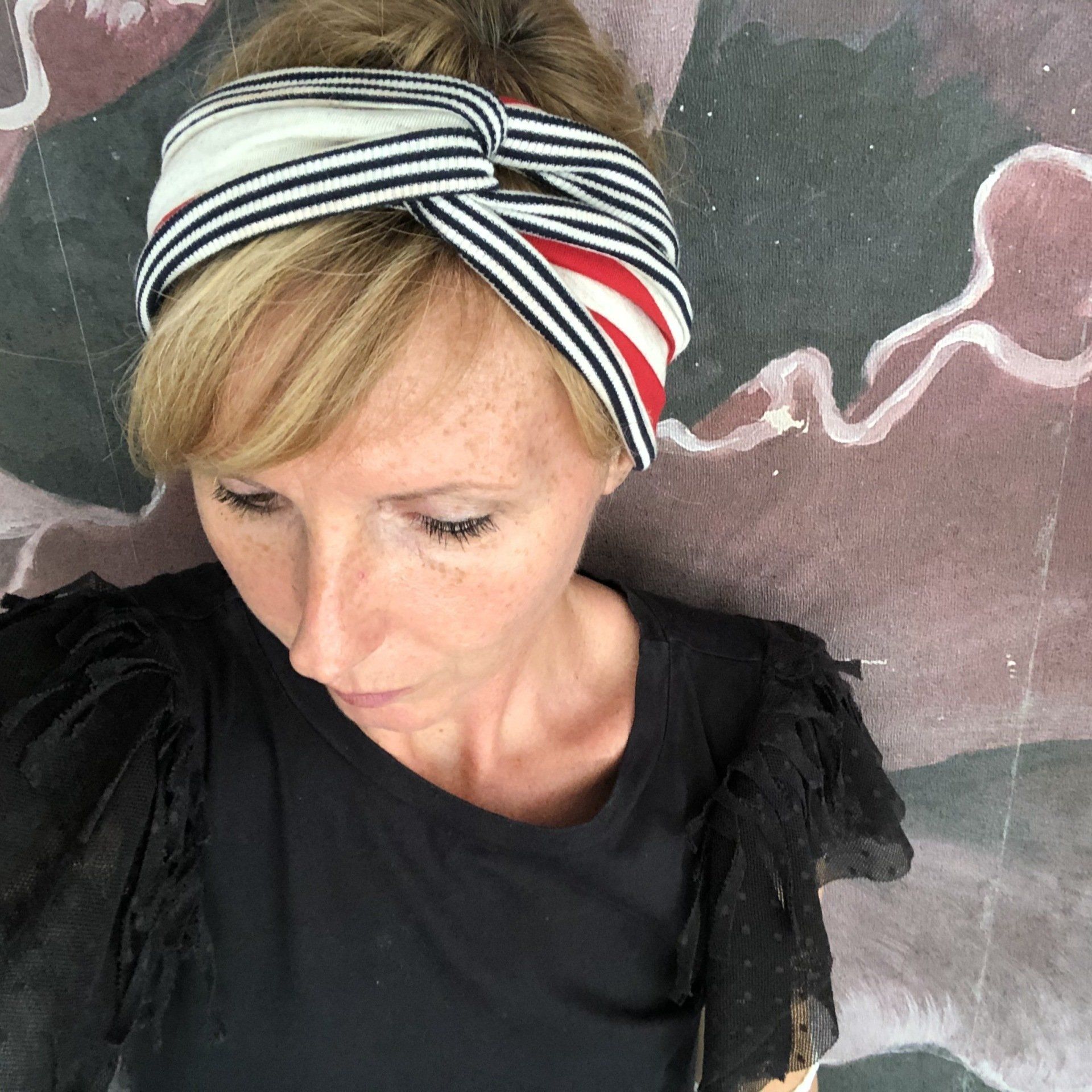 Persona con maglietta nera e fascia per capelli a righe, che guarda verso il basso contro una parete lavagna.
