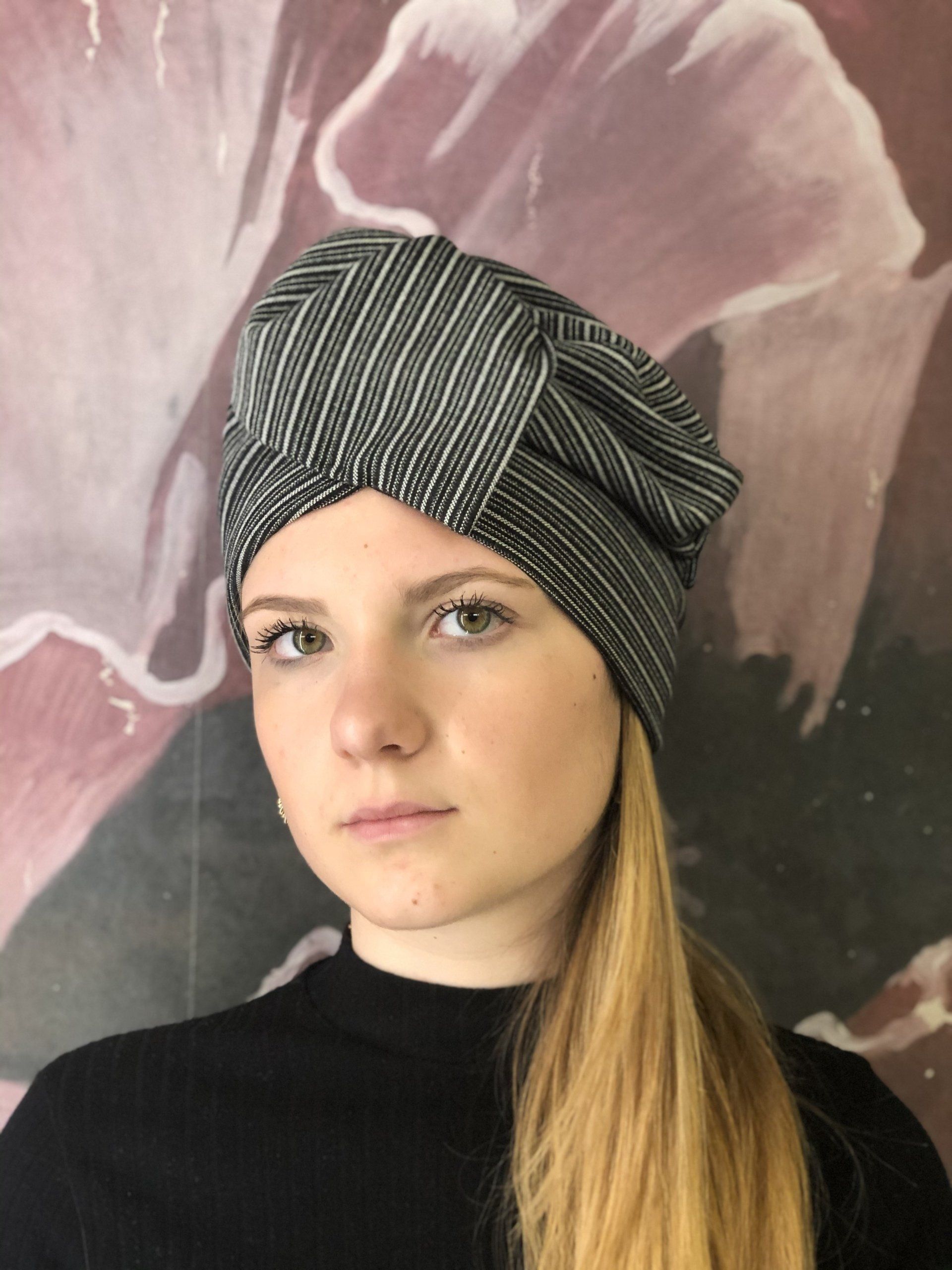 Persona che indossa un turbante a righe bianche e nere e una maglietta nera su uno sfondo floreale.