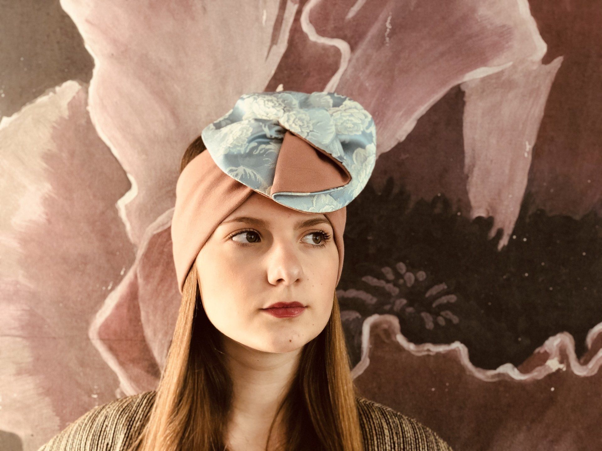 Ritratto di una persona con un foulard rosa e un fiocco blu, su uno sfondo floreale dipinto.