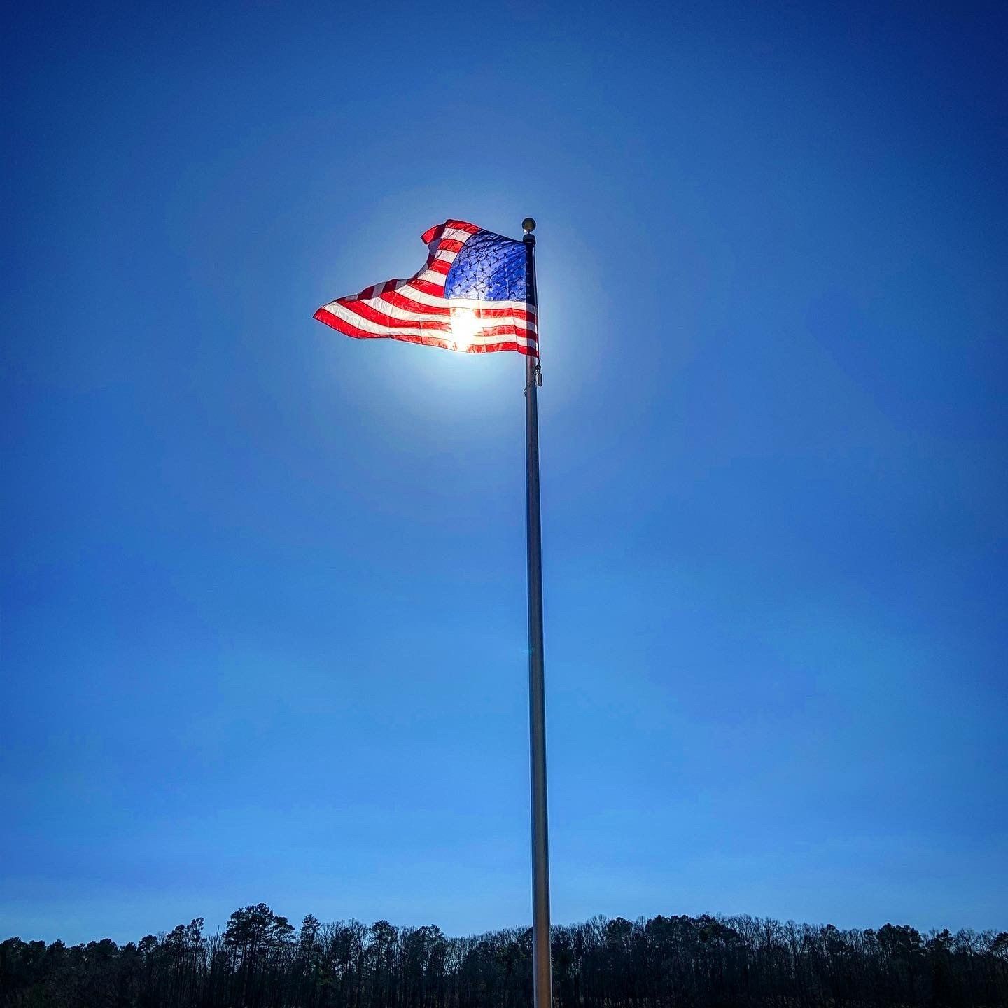 An american flag is flying in the wind against a blue sky