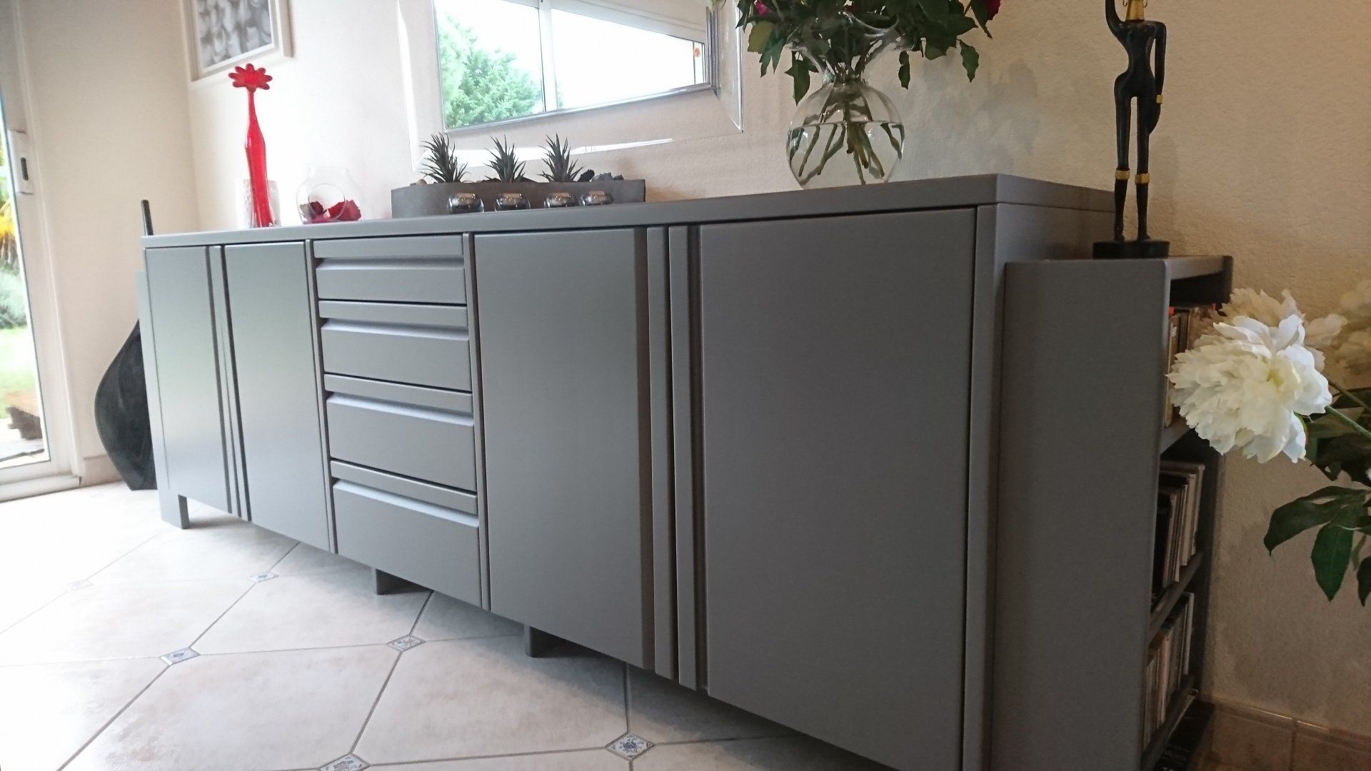 Une longue armoire grise avec tiroirs et portes dans un salon.