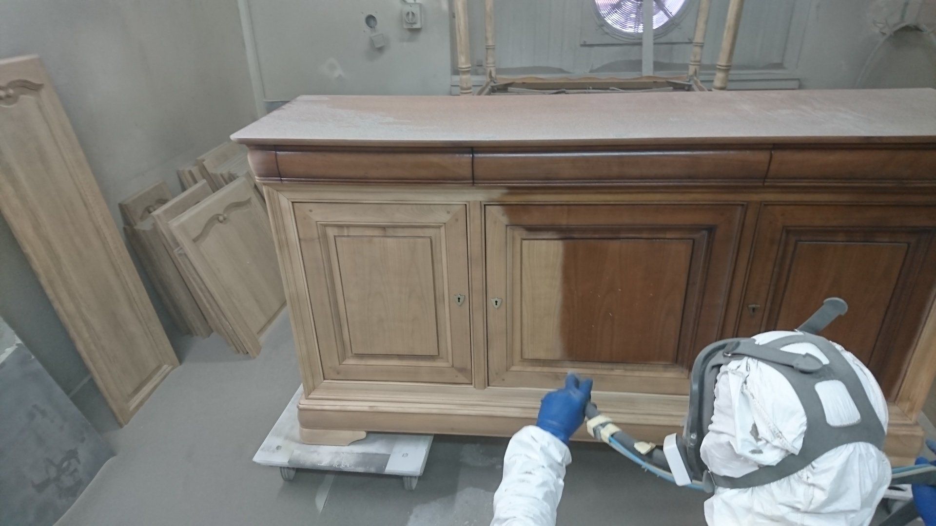 Une personne portant un masque à gaz peint une armoire en bois.