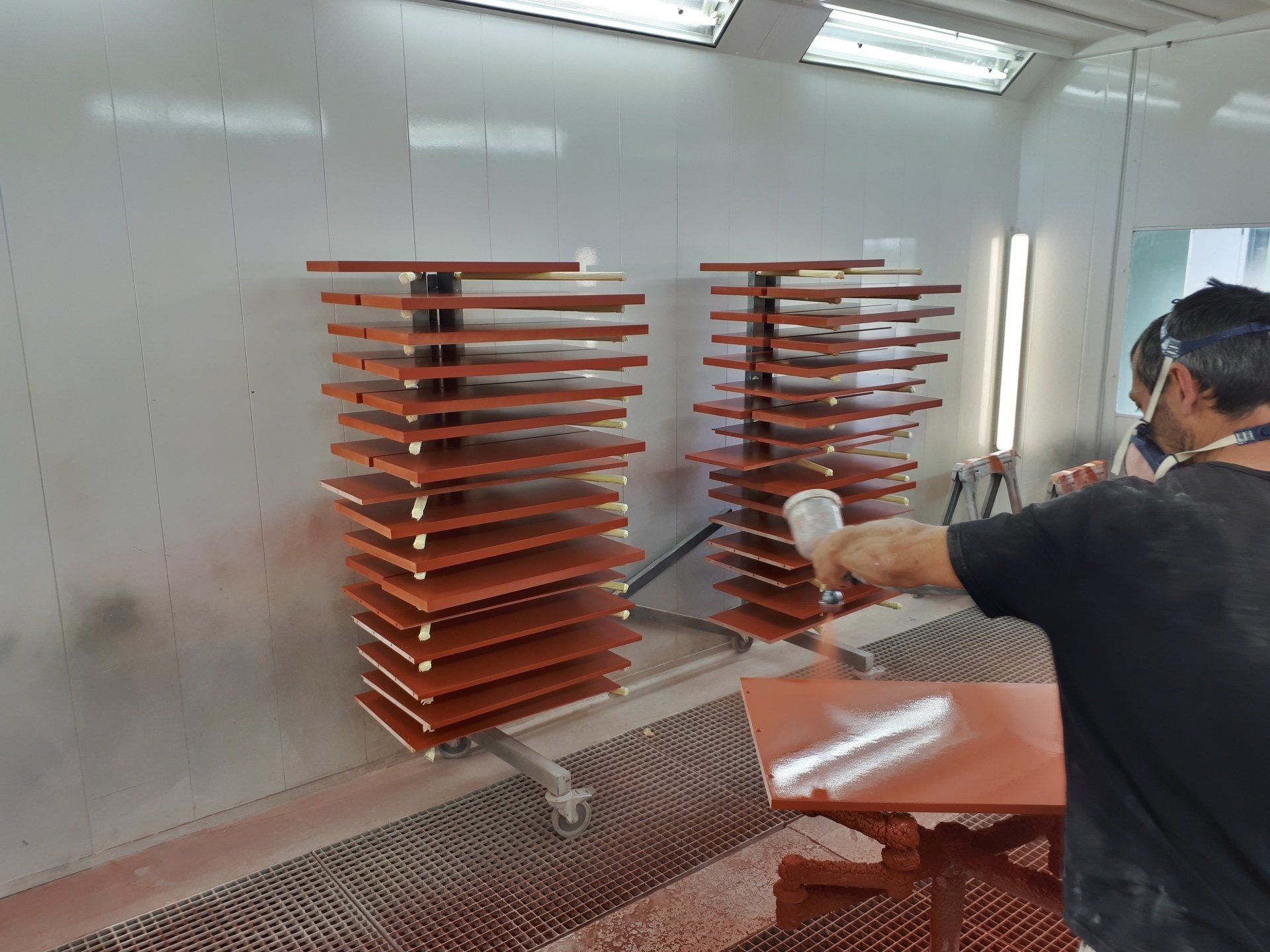 Un homme peint au pistolet une table dans une cabine de peinture.