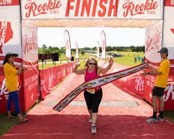 Een vrouw passeert de finish van een Tri-race. Ze wordt aangemoedigd door twee vrijwilligers.