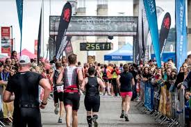 Lopers passeren de finishlijn van een race, onder toeziend oog van toeschouwers. De finishklok staat op 2:56:11.