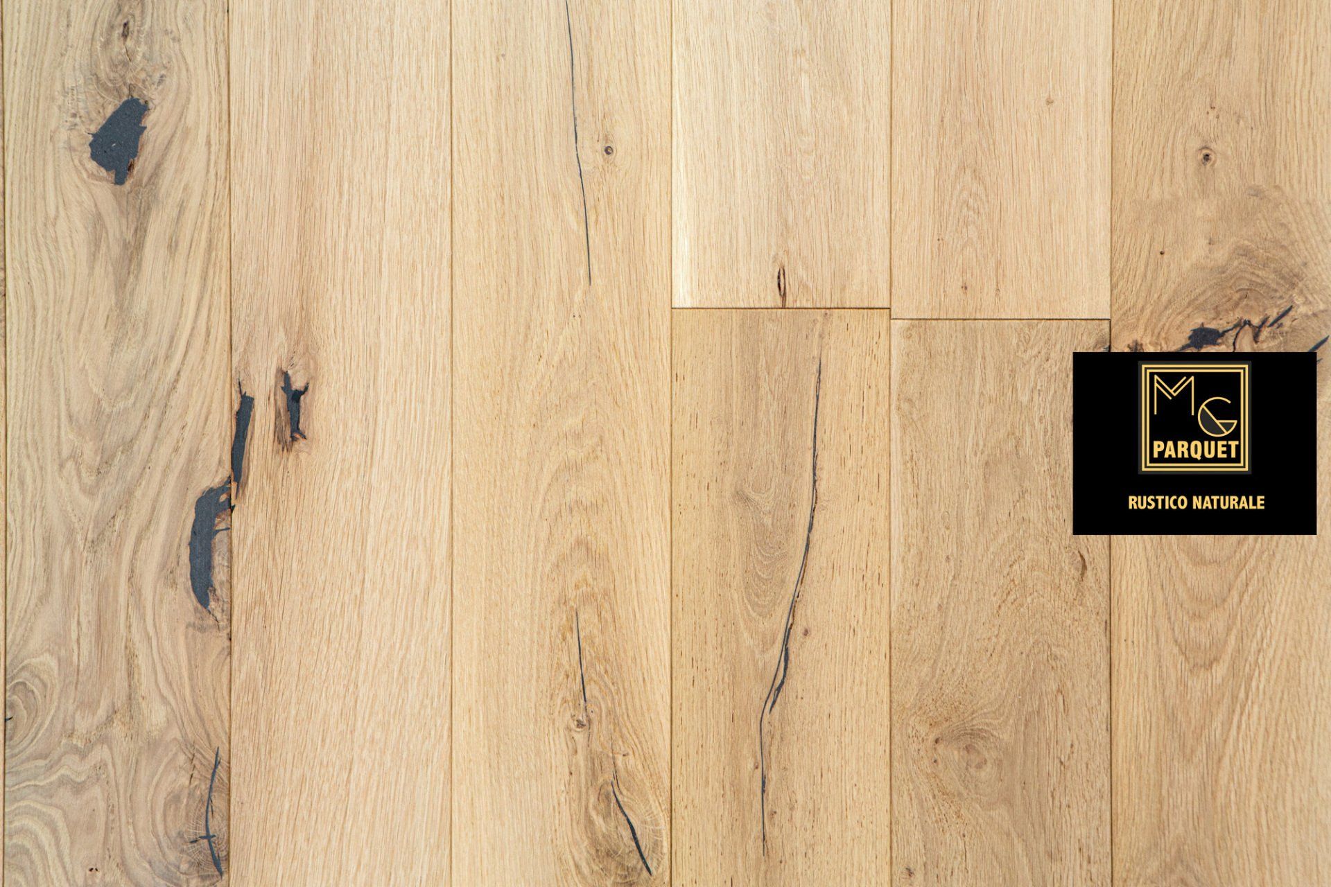 Pavimento in legno chiaro con nodi e crepe scuri, logo parzialmente visibile nell'angolo destro.
