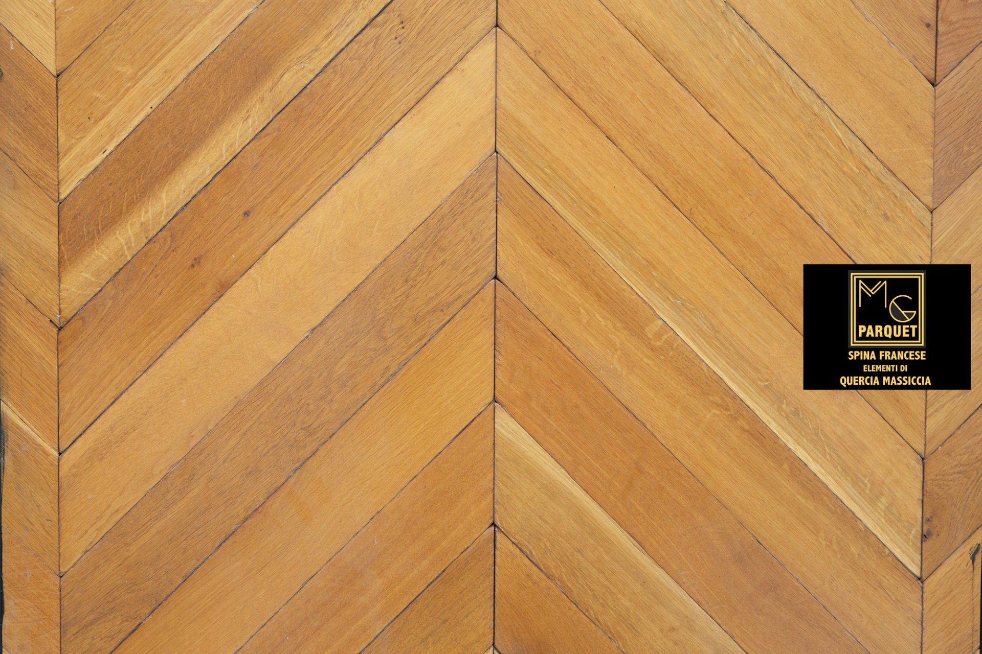 Pavimento in legno con motivo a spina di pesce e cartello nero.