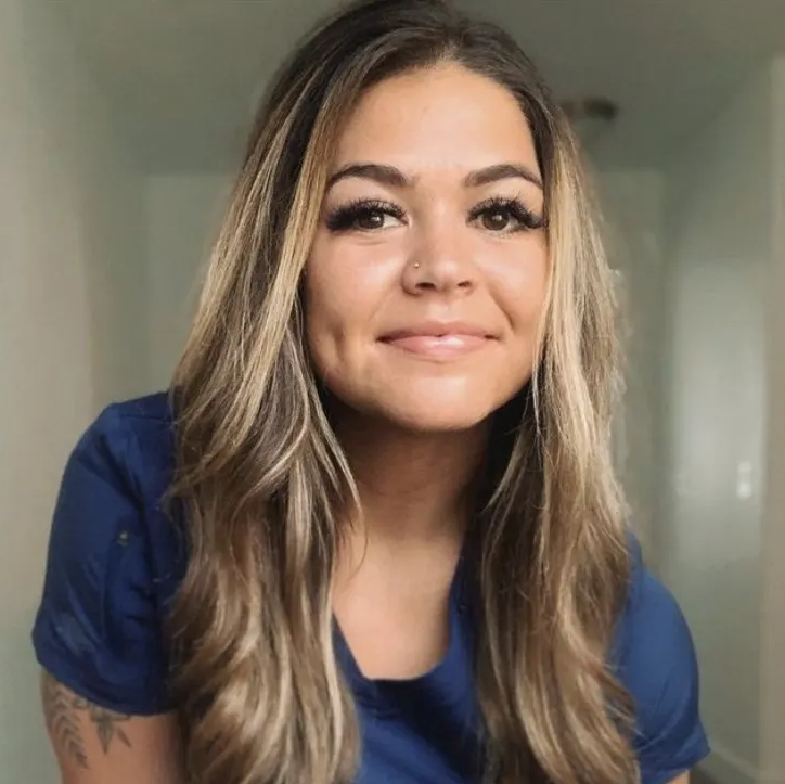 A woman with long hair is wearing a blue shirt and smiling.