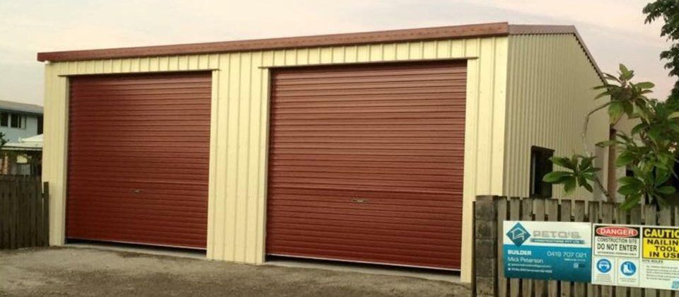 A garage with two red garage doors is behind a fence.