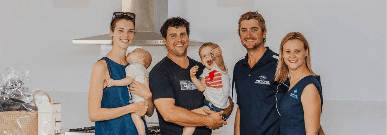 A group of people standing next to each other in a kitchen holding babies.