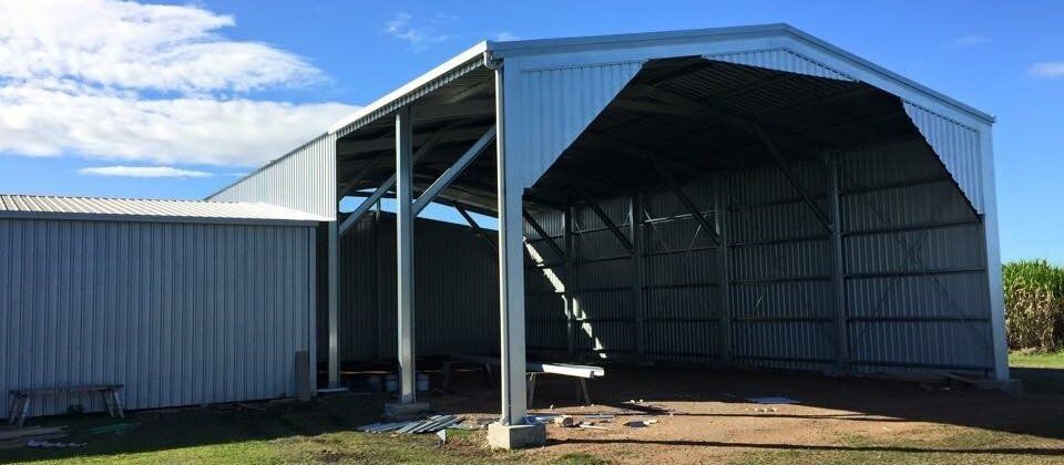 A large metal building is being built on a lush green field.