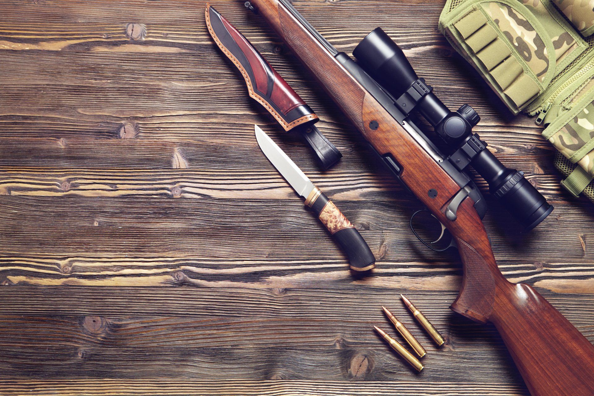 A gun with an optical sight, a hunting knife on a wooden background