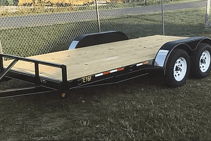 Black flatbed trailer with white fenders parked on grass near a chain-link fence