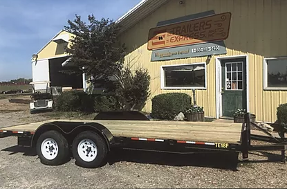 Small black trailer parked outside a yellow building with a green door and sign.