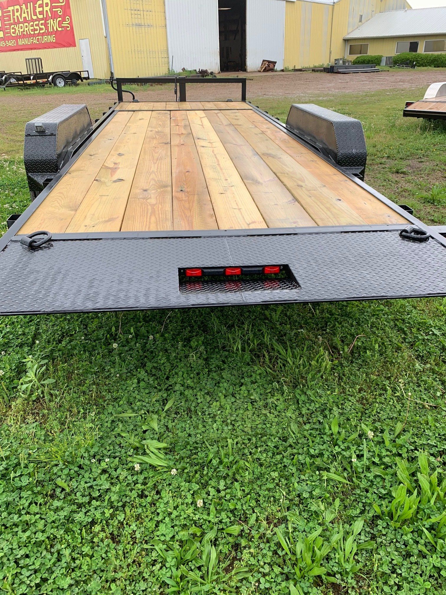 Small utility trailer with wooden deck and gray metal sides on grass, viewed from the rear