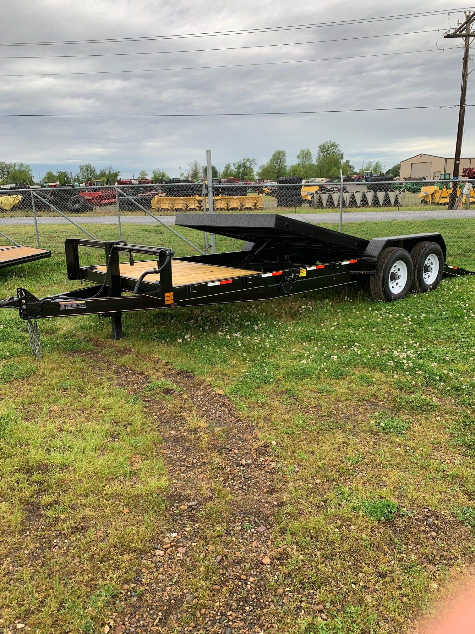 Black dual-axle flatbed trailer parked on grass under a cloudy sky.