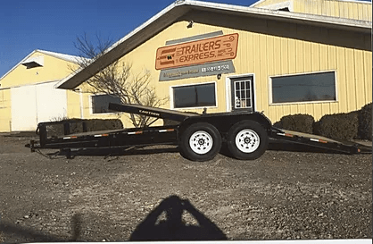 Black flatbed trailer parked in front of a yellow building with a service sign.