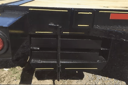 Black utility trailer side with fold-down steps and storage compartments, parked on gravel.