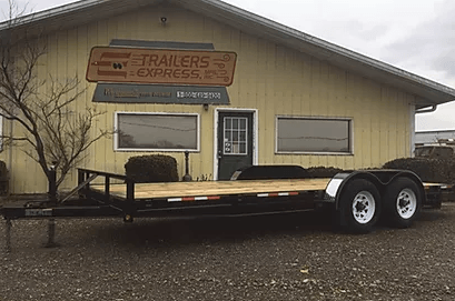 Flatbed trailer parked outside a beige building with a “Railers Express” sign on the wall.