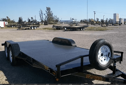 Black flatbed trailer with spare tire parked on gravel lot under a clear sky