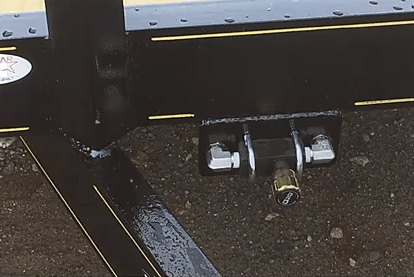 Close-up of a truck hitch and towing connector beneath a black trailer, with wet pavement below