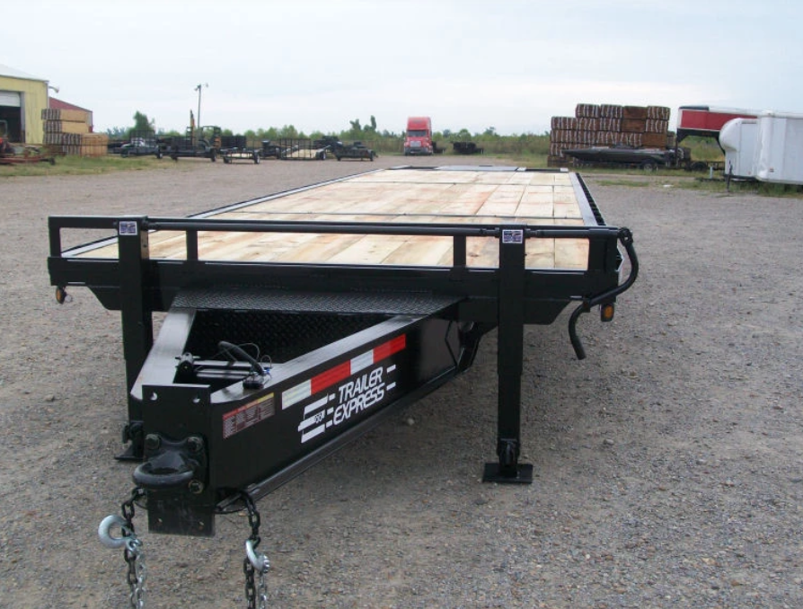 Black flatbed utility trailer with wooden deck parked on gravel in an industrial lot