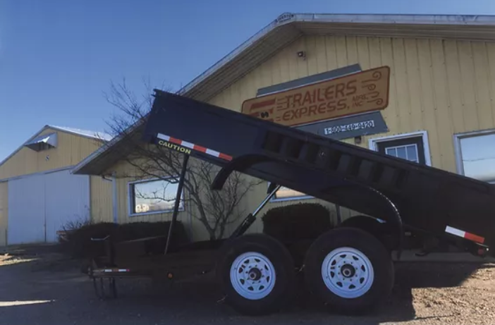 Black dump trailer with raised bed parked outside a trailer shop.