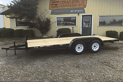 Black dual-axle flatbed trailer parked outside a trailer shop