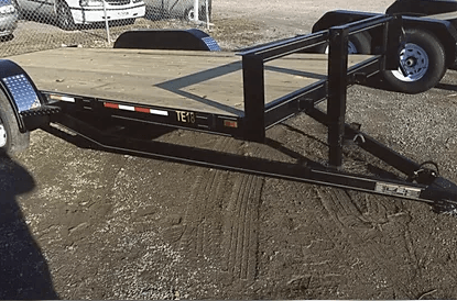 Black utility trailer with two wheels parked on gravel in a yard.