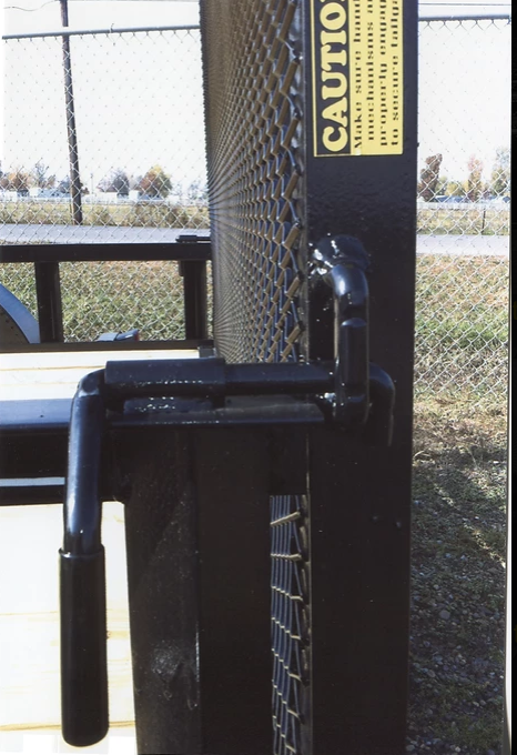 Black gate latch with vertical caution sign on a chain-link fence gate outdoors