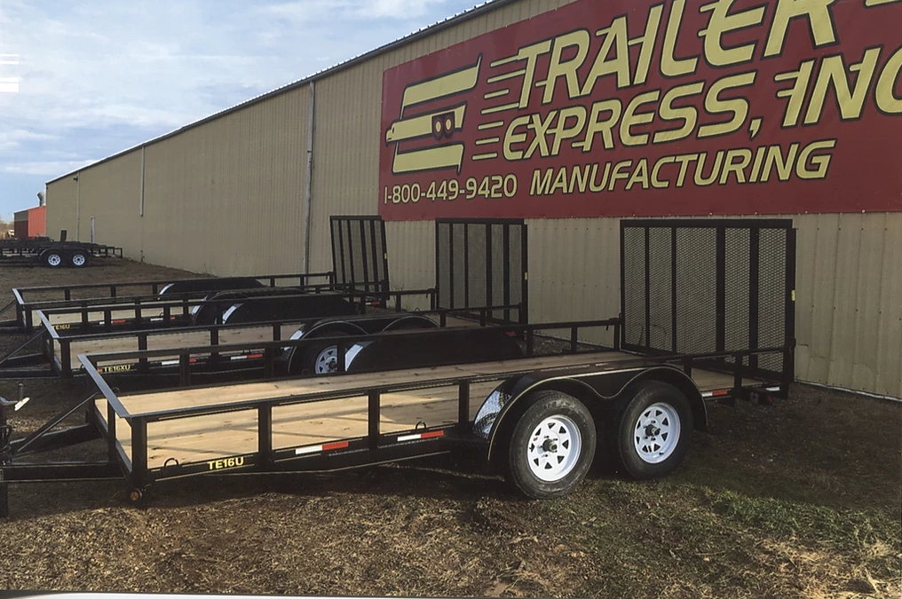 Flatbed trailer parked beside a trailer manufacturing building with a large red sign.