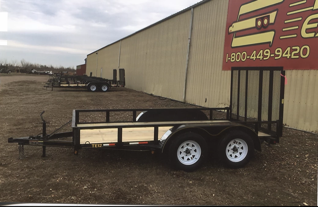 Small black utility trailer beside a tan storage building with a red phone-number sign.