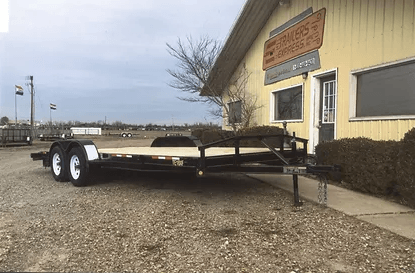 Flatbed trailer parked beside a yellow building on a gravel lot