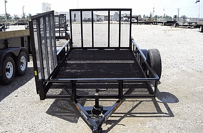 Black utility trailer with metal mesh sides and hitch parked on a gravel lot near water.