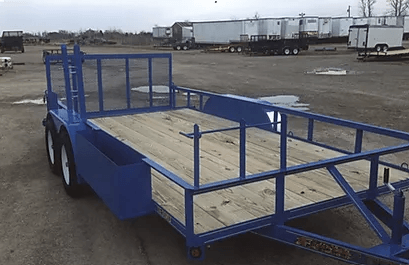 Blue flatbed utility trailer with metal railings parked on a gravel lot