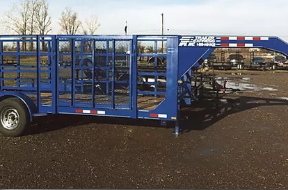 Blue livestock trailer parked outdoors on a wet lot, with metal cage sides and ramp extended.