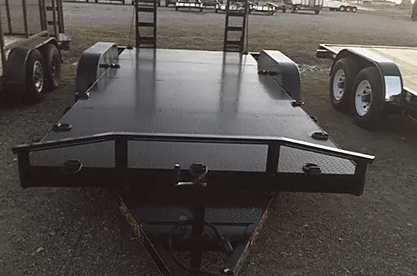 Black flatbed trailer on gravel, front view, with dual wheels and tie-down points.