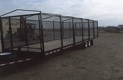 Long flatbed trailer with metal mesh sides parked on a gravel lot under a cloudy sky