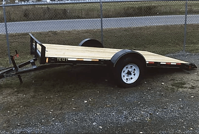 Wooden utility trailer with white wheels parked on grass beside a chain-link fence
