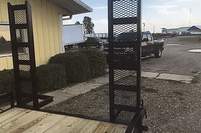 Black metal carts on a wooden deck beside a yellow building and parked trucks in a gravel lot.