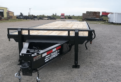 Black flatbed gooseneck trailer parked on gravel lot with a wooden deck and jack stand.